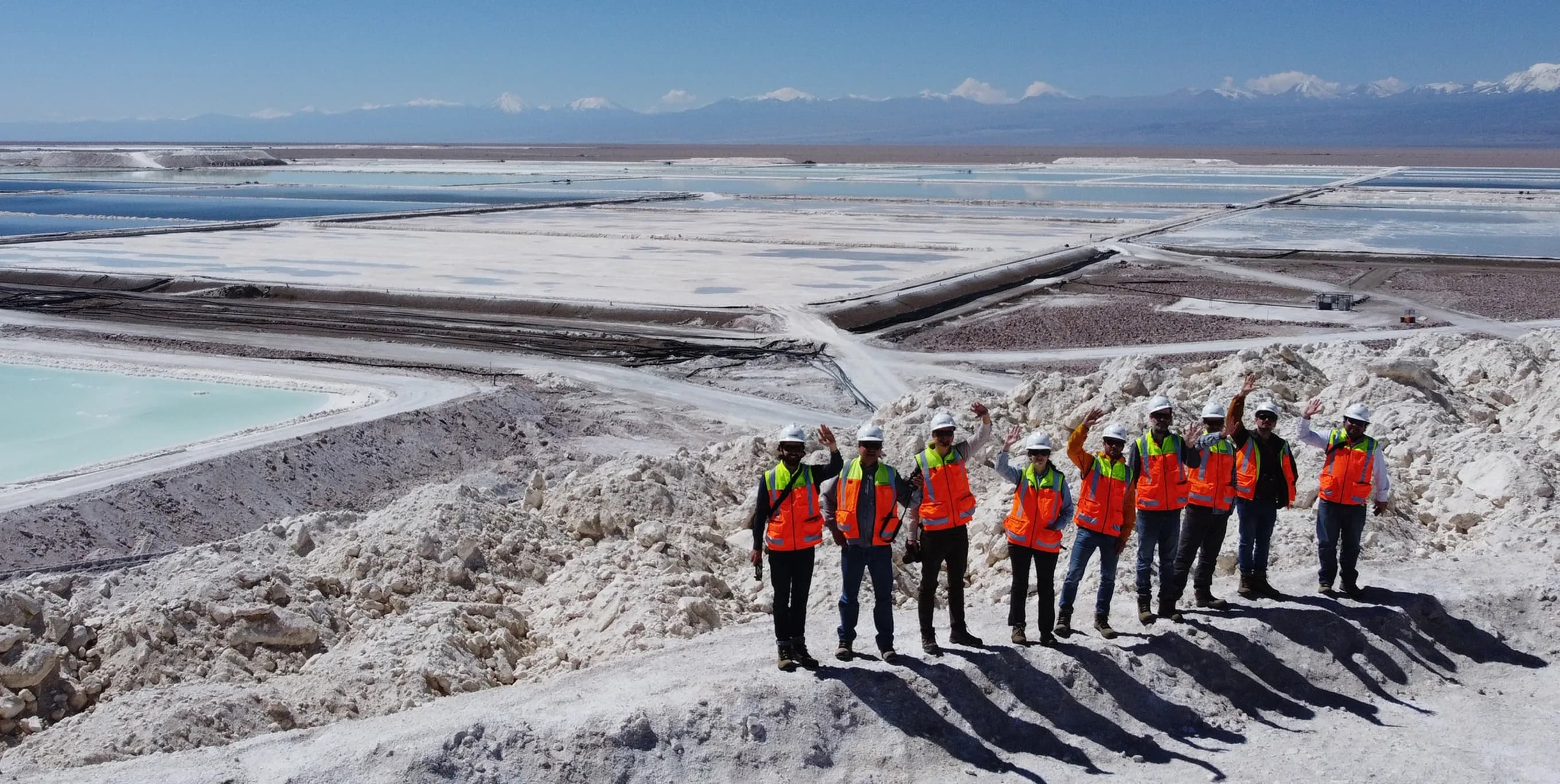 An aerial view of a salt flat, with a line of workers in high-visibility jackets standing on the ridge